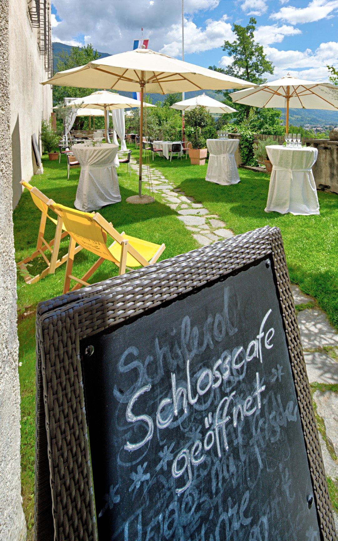 Außenbereich Schlosscafé, Terrasse mit Stehtischen und Liegestühlen, Tafel mit "Schlosscafé geöffnet"